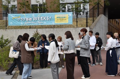 「クラブ新歓WEEKS!」の告知の前でビラ配り